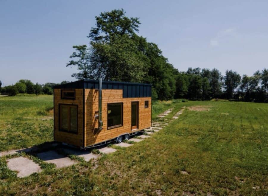 Compact tiny house with modern wooden exterior and large windows, situated in a lush green landscape.