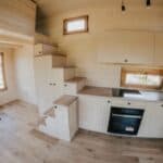 Compact tiny house kitchen with natural wood finishes and modern appliances.
