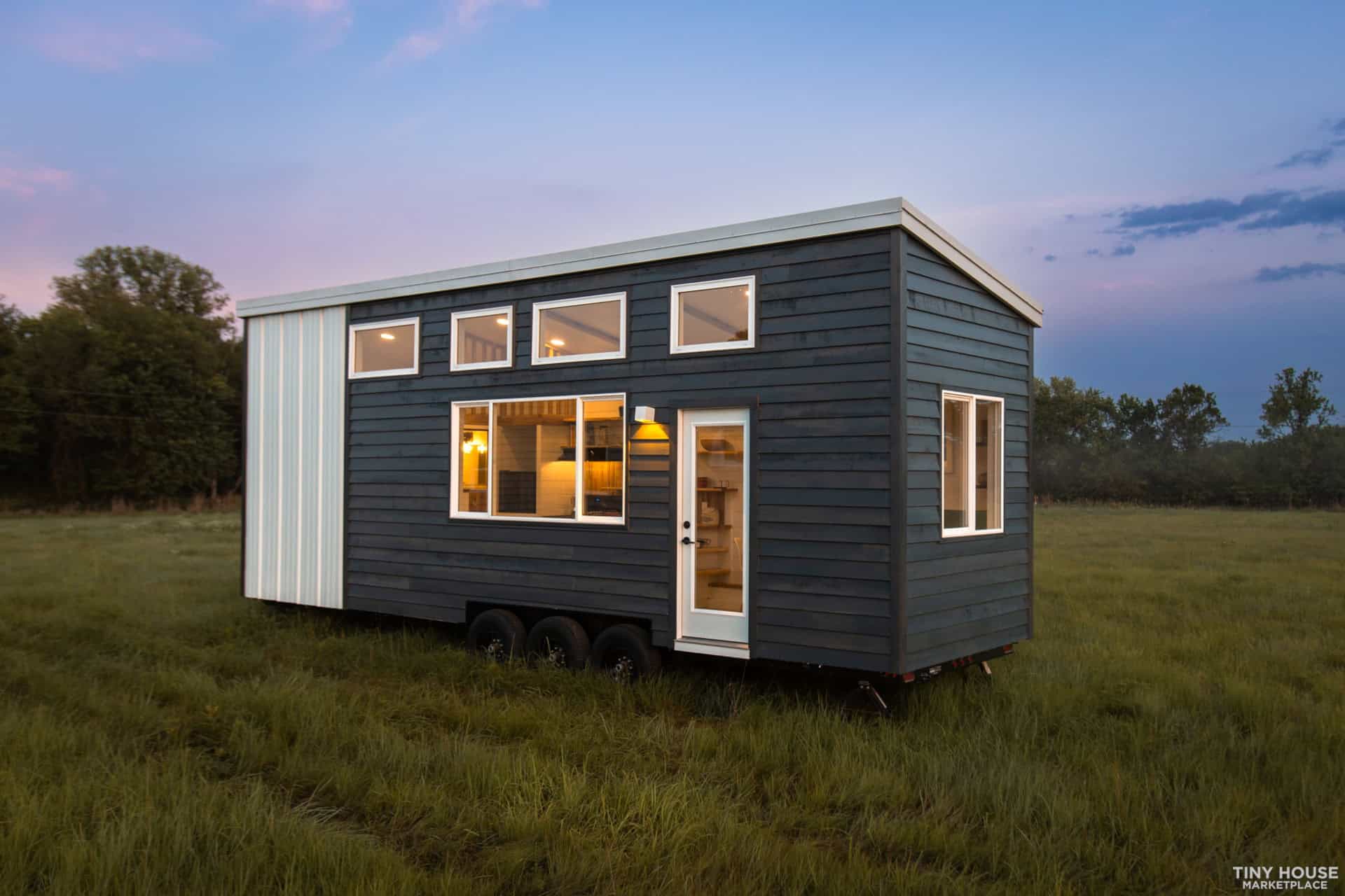 The Elderberry tiny house glowing from inside at dusk in an open field
