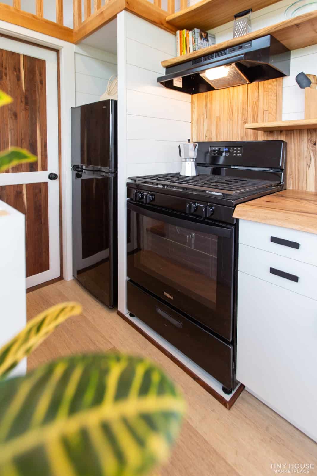 Black 30-inch gas range with oven and hood fan beside a black refrigerator in the Elderberry kitchen