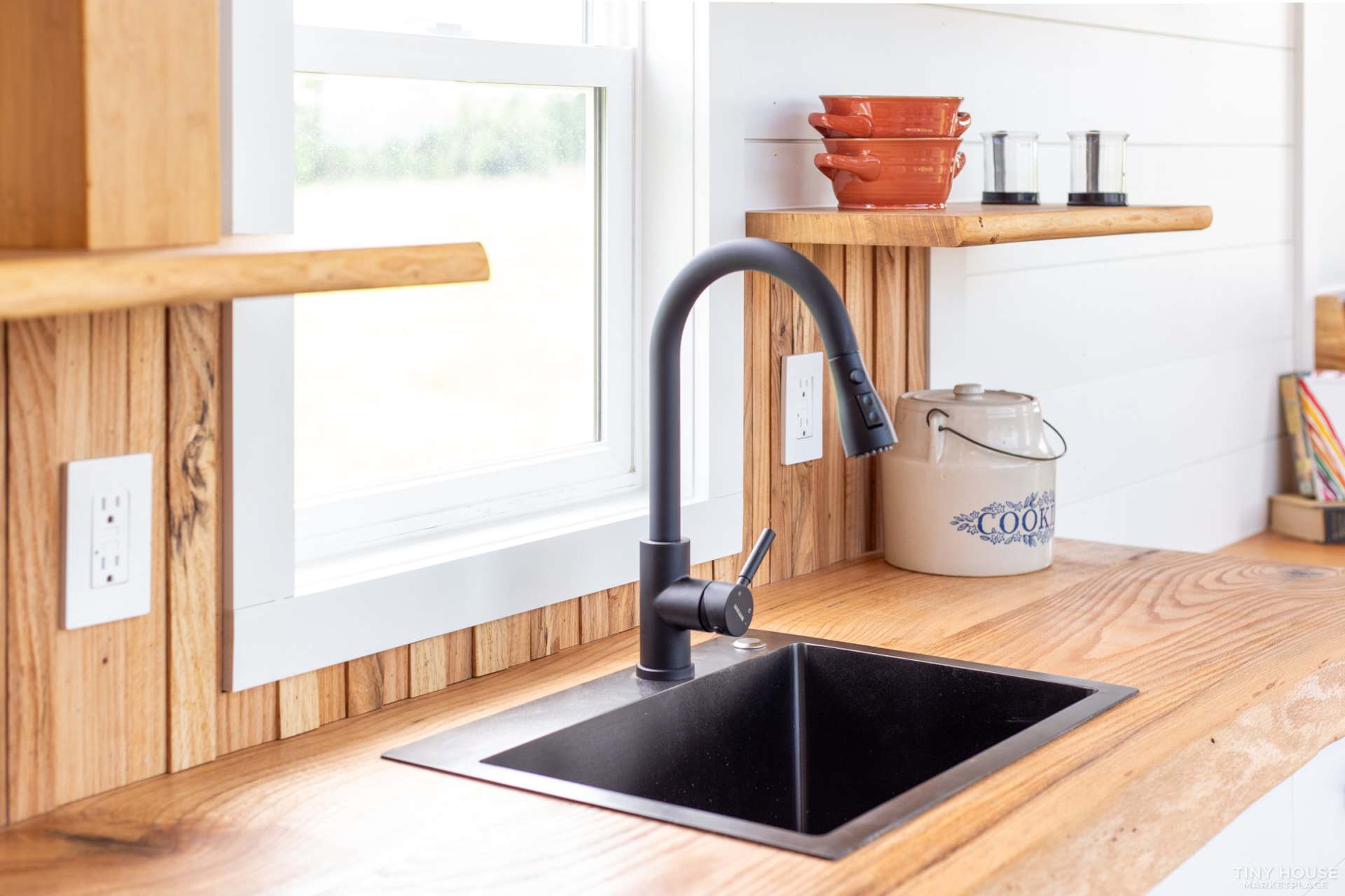 Black kitchen sink and pull-down faucet under a window with live-edge oak shelves in the Elderberry