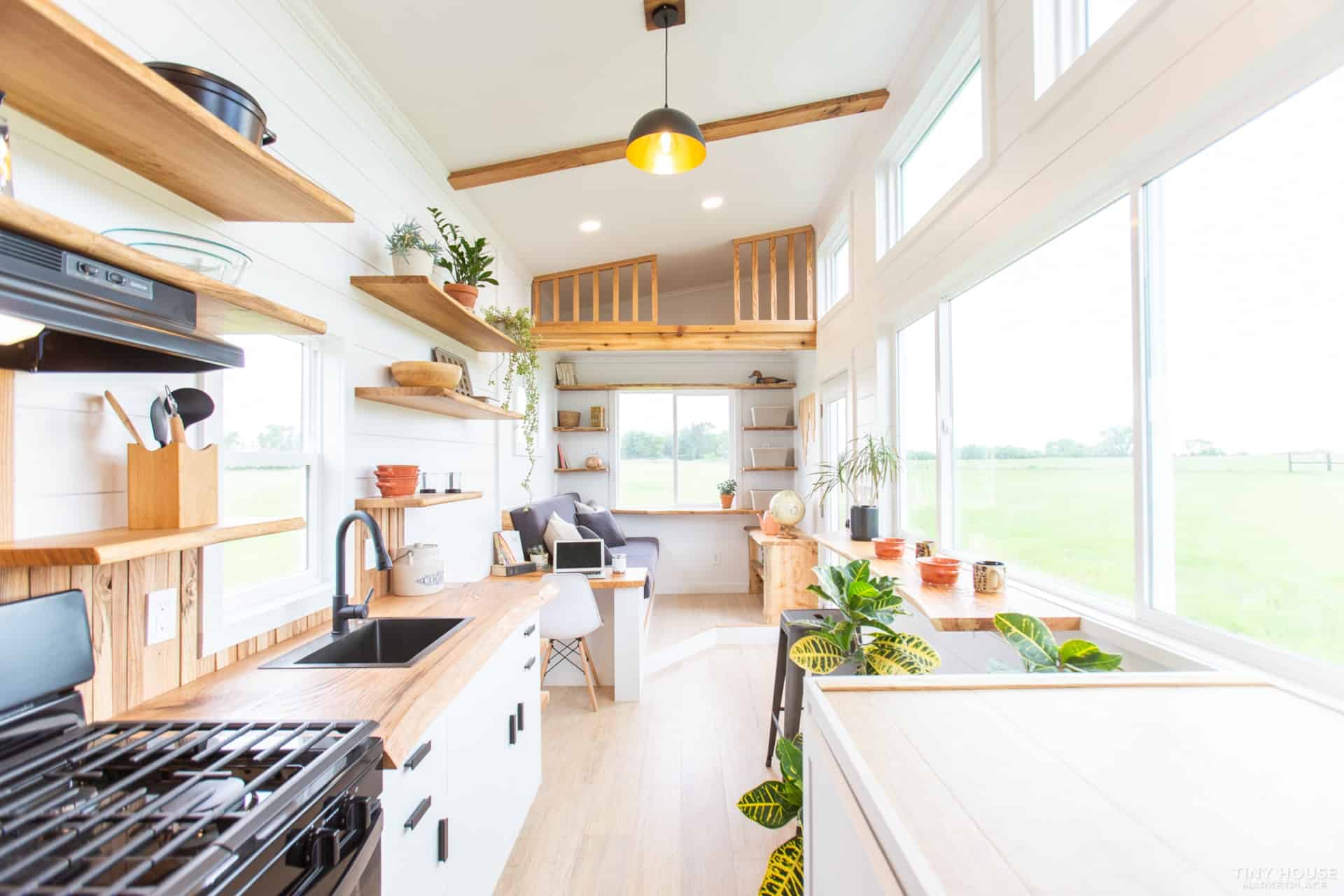 Wide view of the Elderberry kitchen with oak counters, gas range, open shelving, and the living room beyond