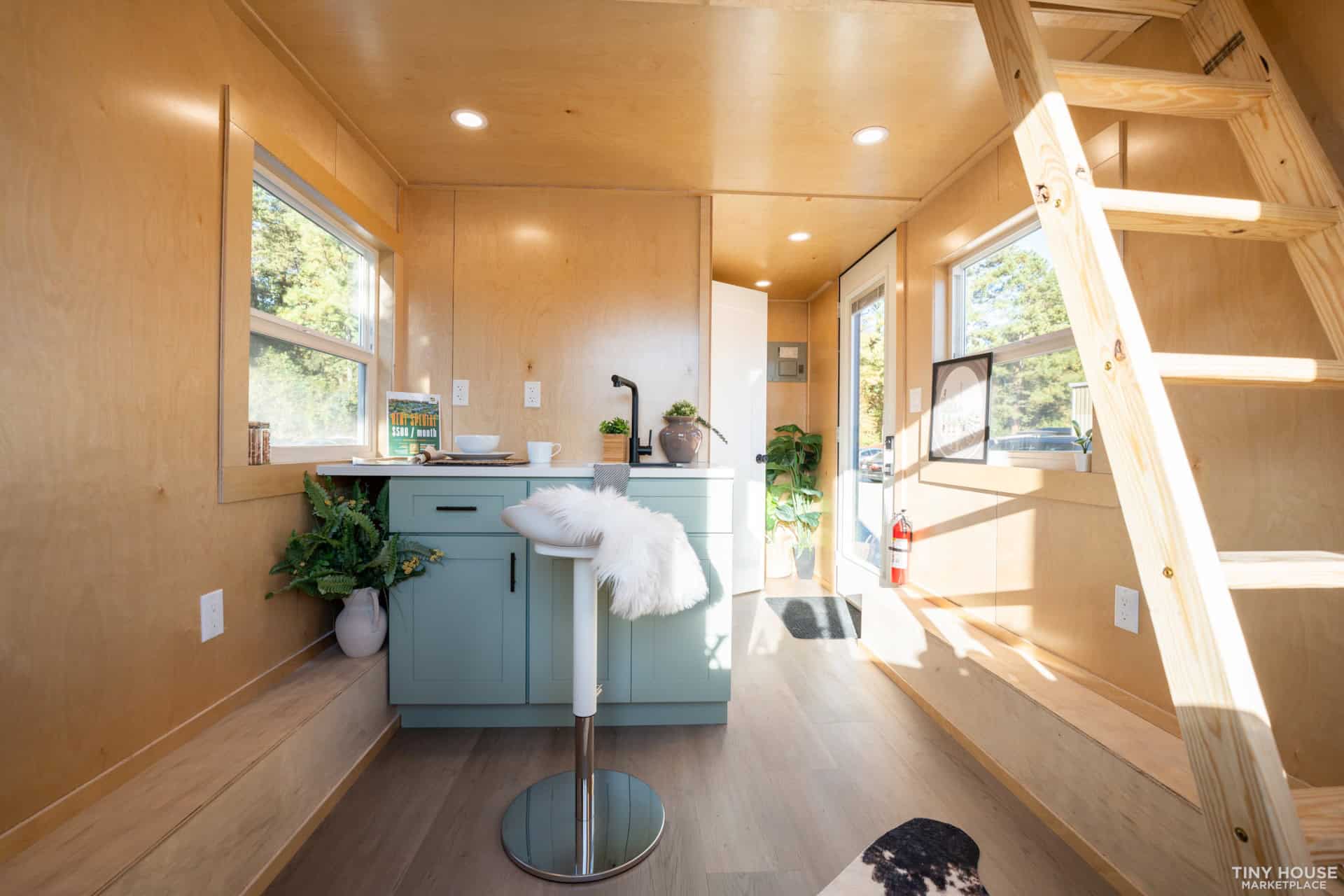 Compact tiny house kitchen with natural wood finishes and large windows for bright, open living spac.