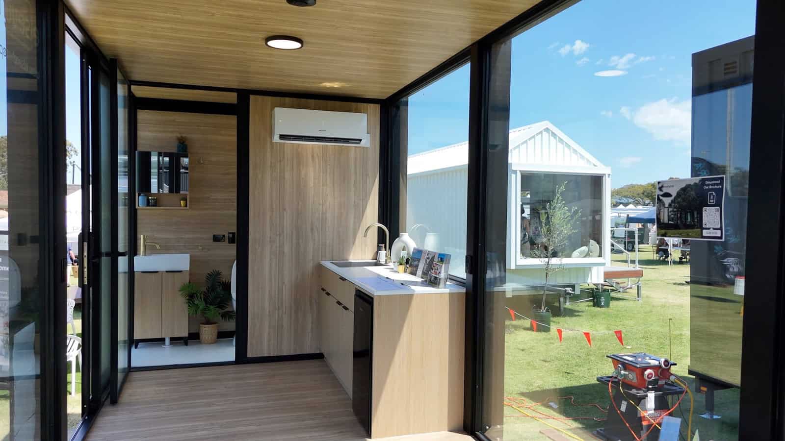 Interior of the Elsewhere Pods 6m Tiny Home showing the kitchen run, split system air conditioner, and bathroom beyond