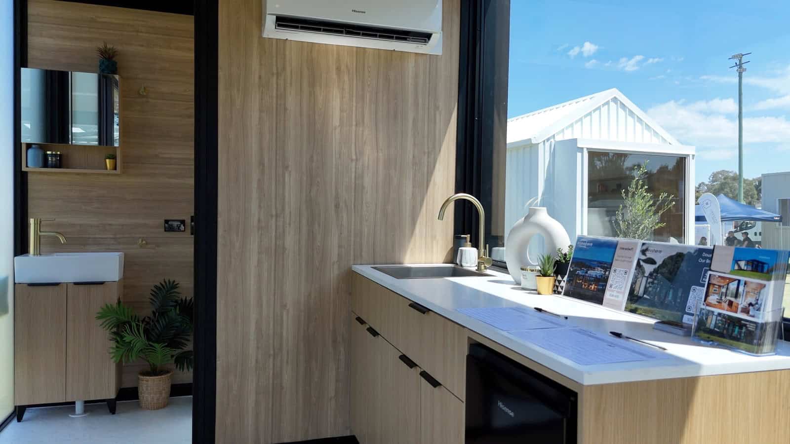 Kitchen detail with brushed brass Yabby tapware, white benchtop, and integrated bar fridge