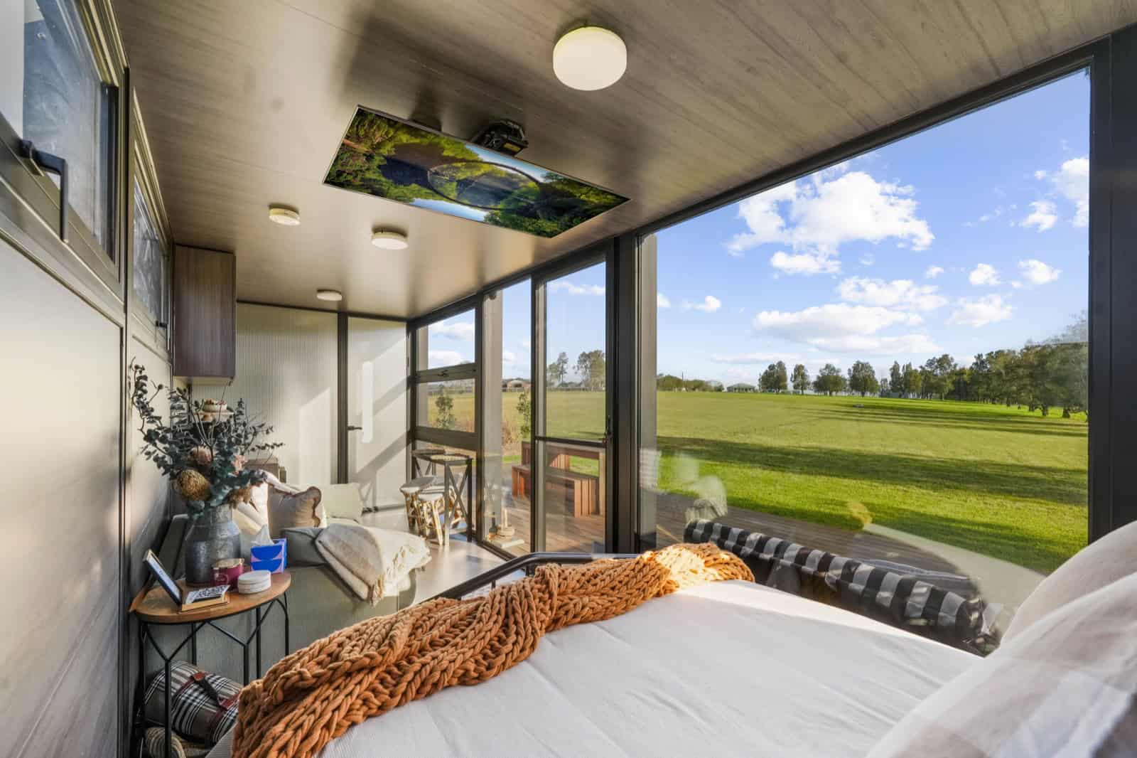 View from the bed of the 8m pod across farmland, with a projector recessed into the ceiling