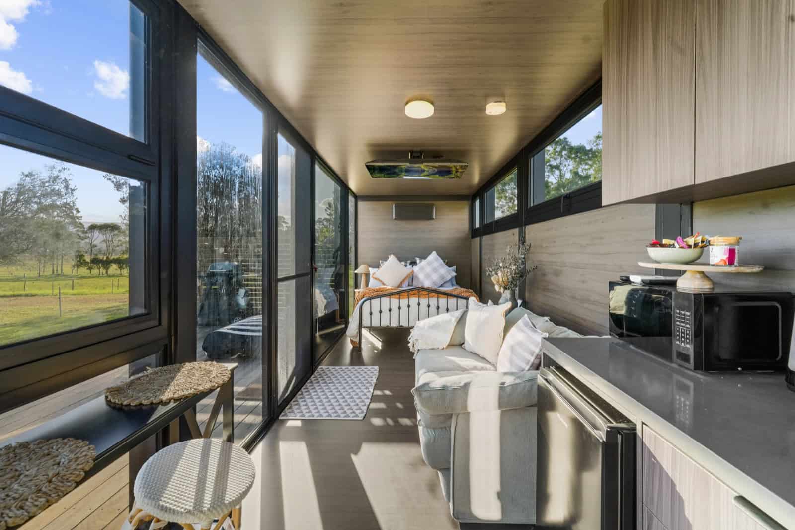 Interior of the 8m pod showing the kitchen run, sofa, and queen bed in three distinct zones