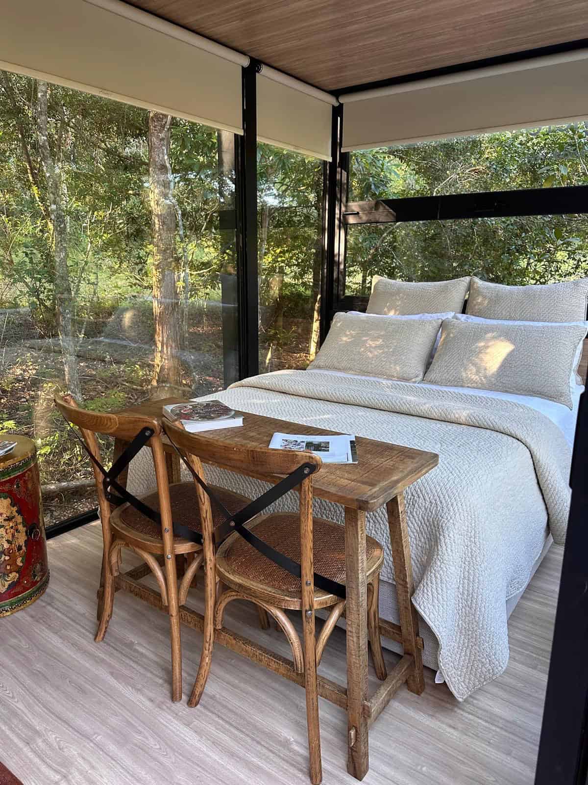 Timber console table and two cafe chairs at the foot of the bed facing full-height glazing