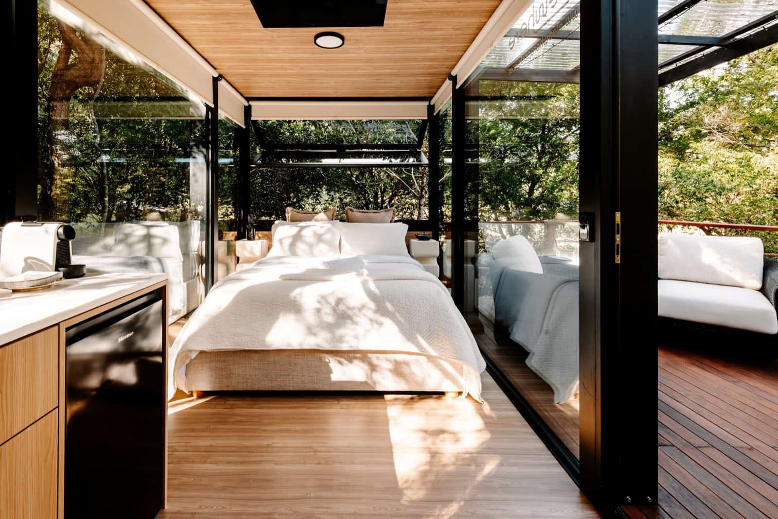 Interior of the Peachester pod with a queen bed surrounded by full-height glazing and rainforest views