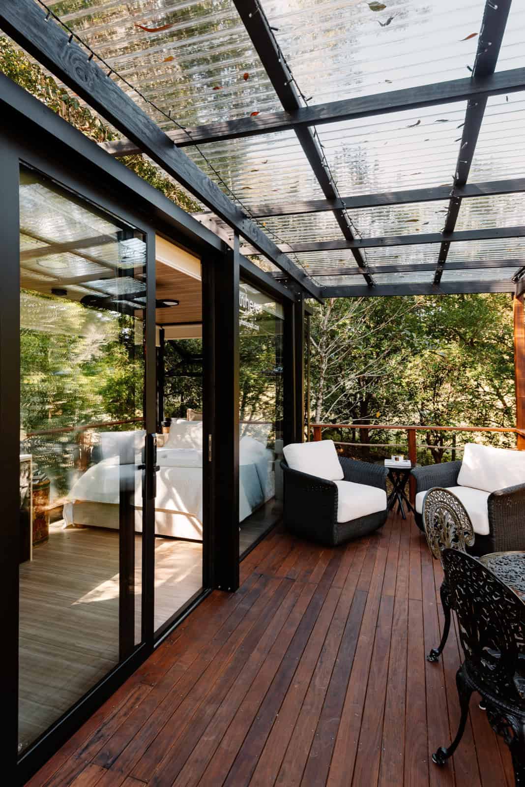 Covered deck with polycarbonate pergola roof, wicker armchairs, and the bedroom visible through the slider