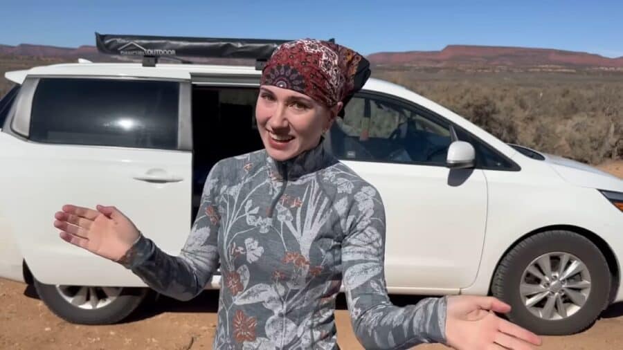 Woman smiling outside her minivan in a desert landscape, showcasing van life setup.