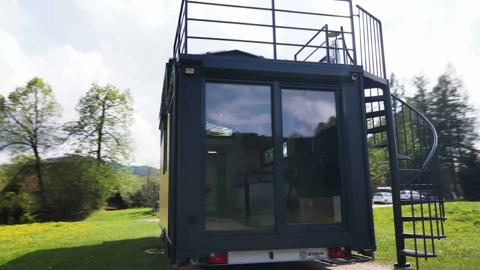 Rear of the yellow Erica build with a large black-framed sliding glass door and a spiral staircase rising to the rooftop terrace