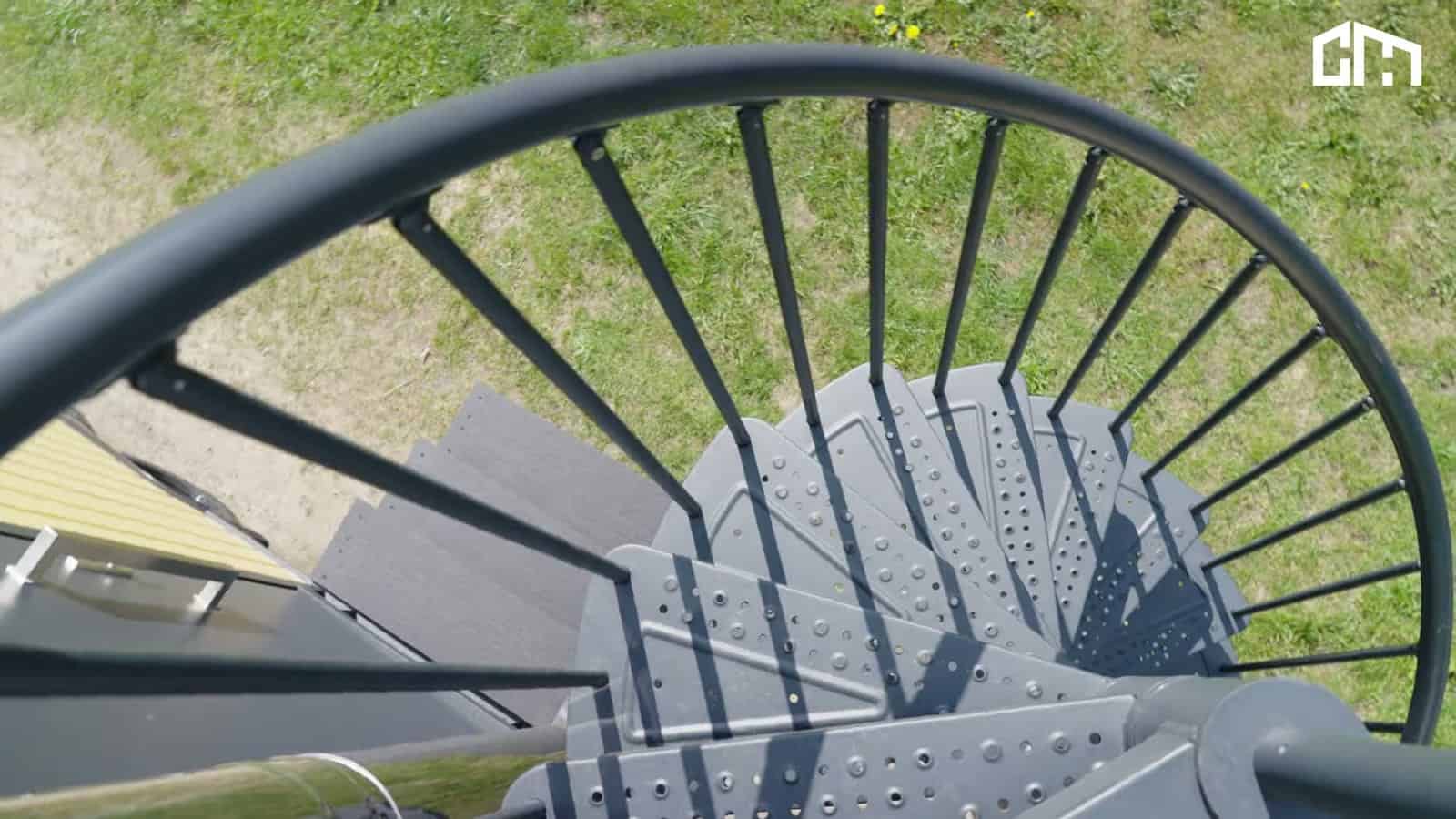 Looking down a dark gray spiral staircase from the Erica's rooftop terrace to the grass below