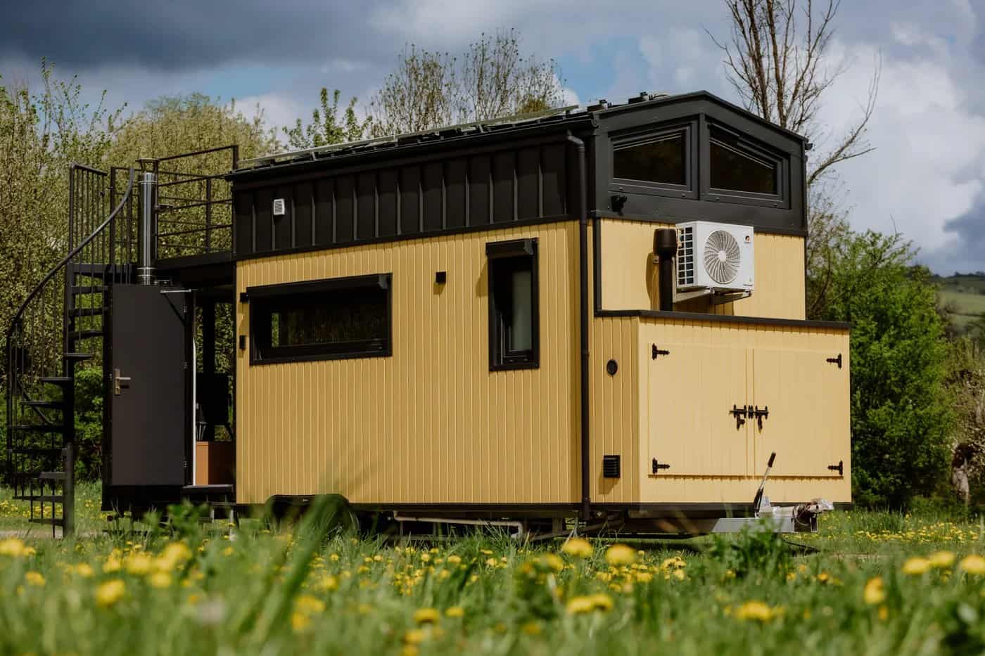 The yellow-and-black build of the Erica tiny house with a gable roof and rooftop terrace