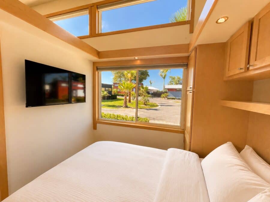 Bedroom of the Traveler XLS Wide with a wall-mounted TV, clerestory window, and a large window letting in natural light.