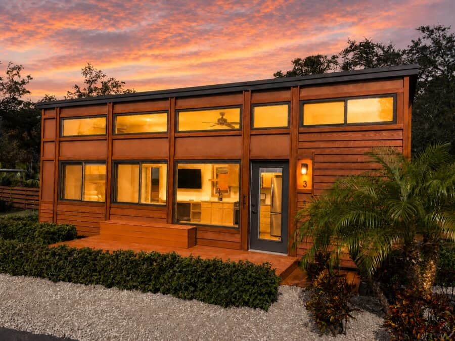 Pre-owned ESCAPE Traveler XLS Wide tiny house at sunset with stained cedar siding, metal accents, a private deck, and landscaping at The Village in Tampa Bay, Florida.