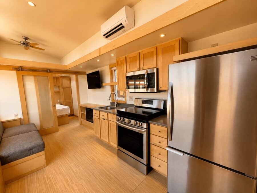 Large tiny house kitchen with stone countertops, stainless french-door fridge, range, microwave, and a sliding barn door to the bedroom.