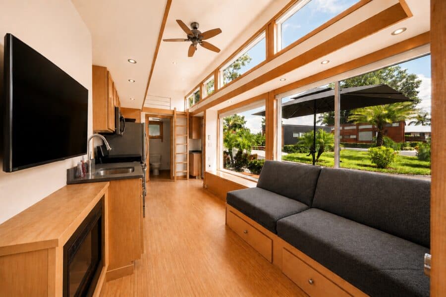 Open living area of the ESCAPE Traveler XLS Wide with a fold-flat storage couch, wall-mounted TV, electric fireplace, and clerestory windows.