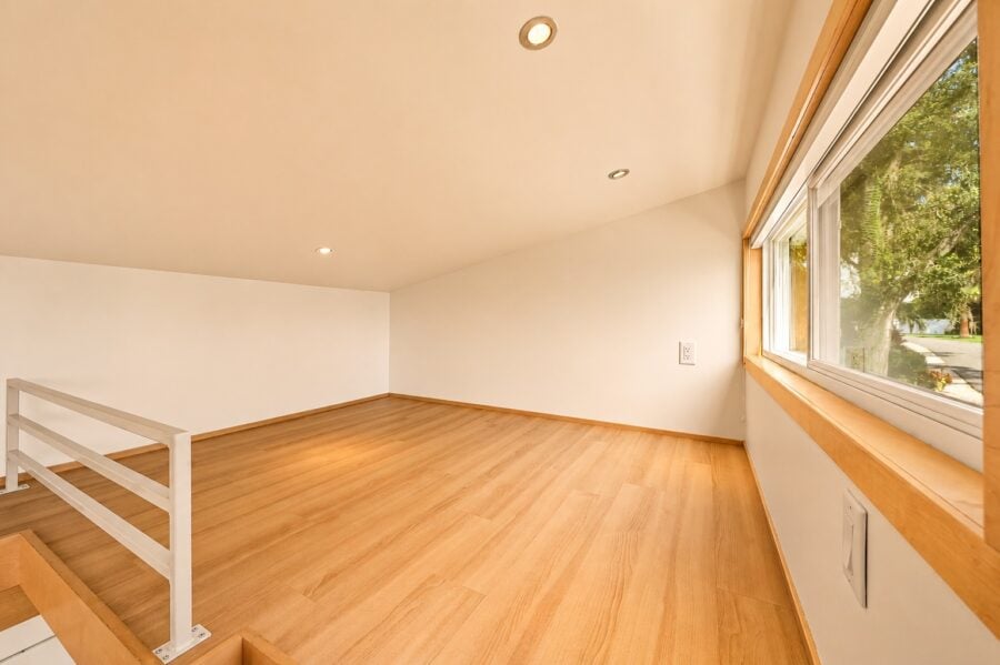 Bright upstairs loft in the Traveler XLS Wide with wood floors, a railing, large window, and vaulted ceiling.