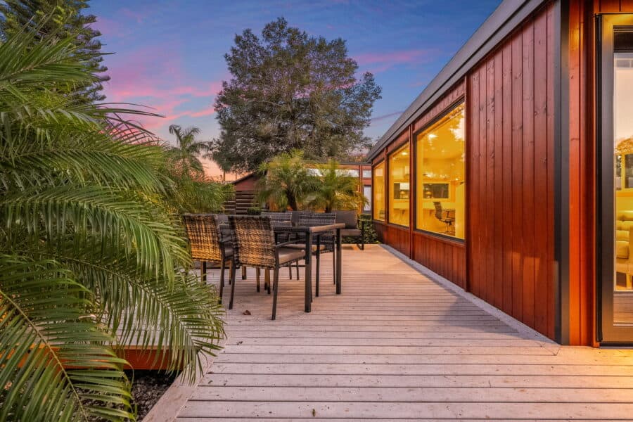 Private wood deck with an outdoor dining set beside the Traveler XLS Wide at dusk, surrounded by tropical landscaping.