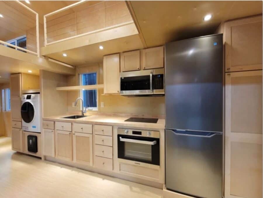 Efficient tiny house kitchen with modern appliances and light wood cabinetry.