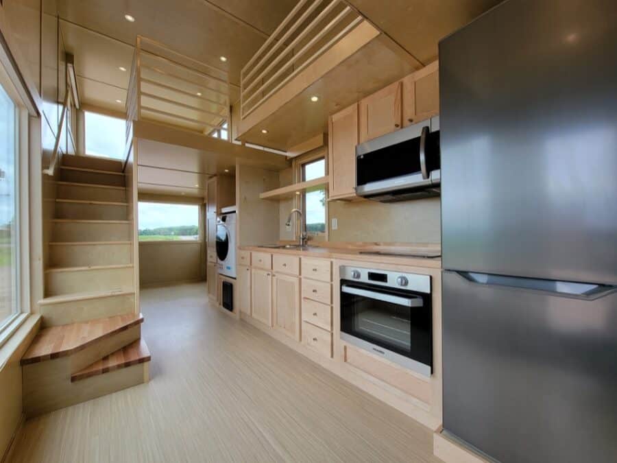 Modern tiny house kitchen with loft, compact appliances, and natural light.