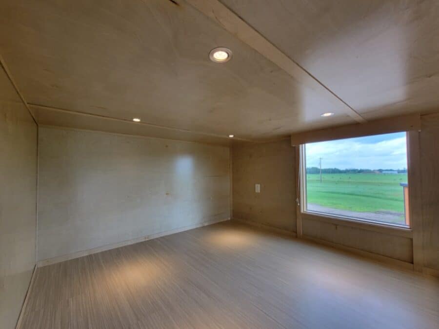 Interior view of a tiny house with wooden walls, ceiling, and flooring, featuring a large window ove.