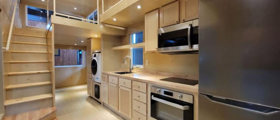 Modern tiny house kitchen with compact appliances and wooden cabinetry.
