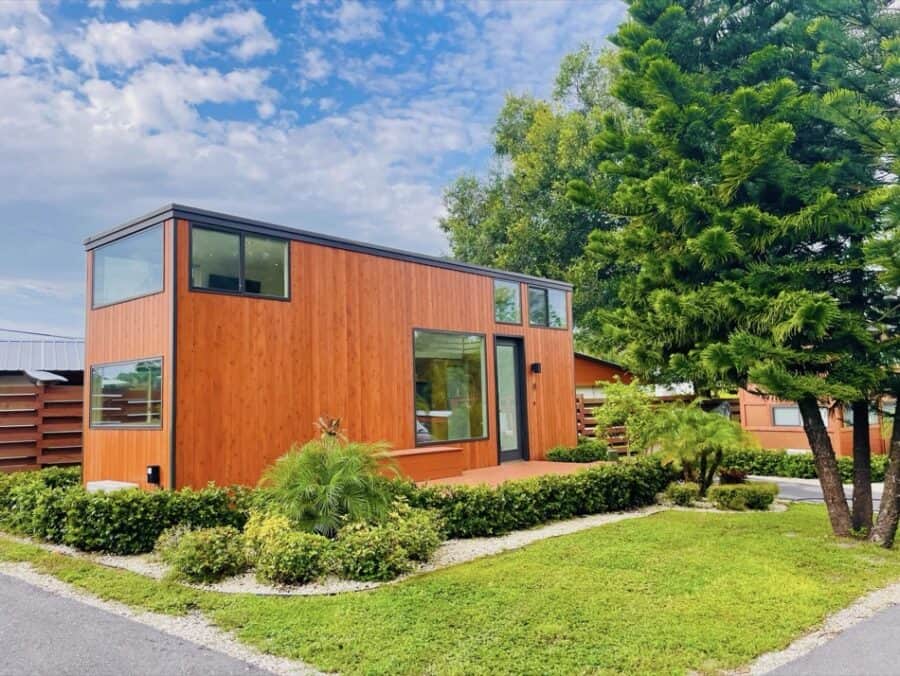 Compact tiny house with sleek wooden siding and large windows, nestled among lush trees and well-mai.