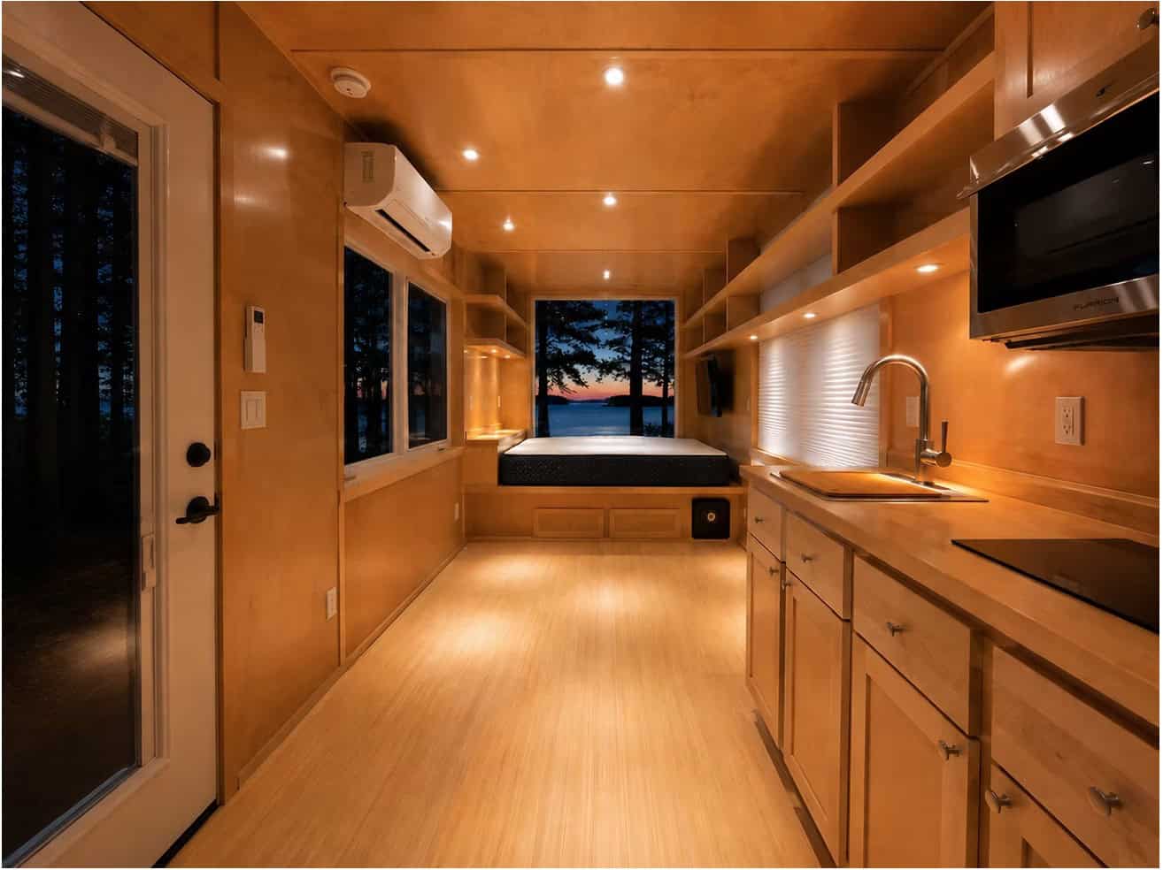 Open studio interior of the Escape eVista tiny house with birch walls, galley kitchen and window bed