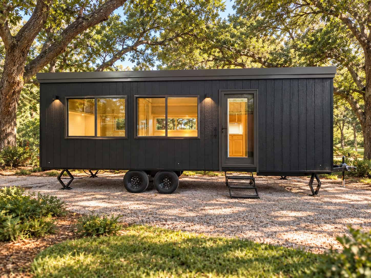 Escape eVista XL Limited tiny house on wheels with black vertical siding parked under oak trees