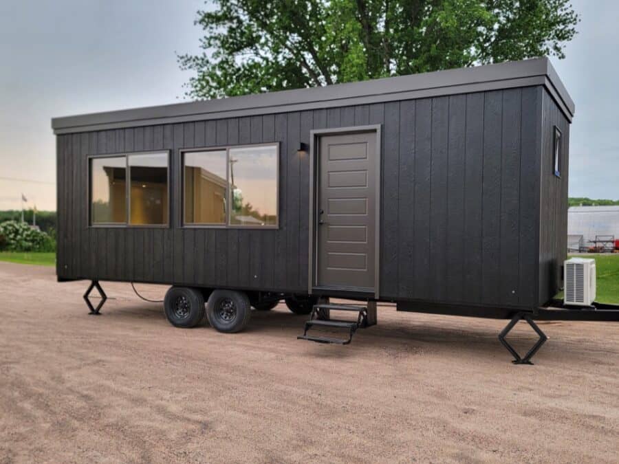 Modern black tiny house on wheels with large windows and outdoor steps, ideal for small space living.