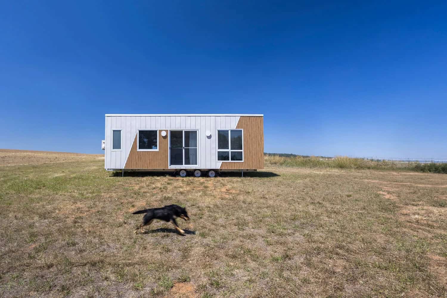 The Esther tiny house sited in an open Australian paddock, showing the full 9-meter side elevation with its white and timber-look cladding
