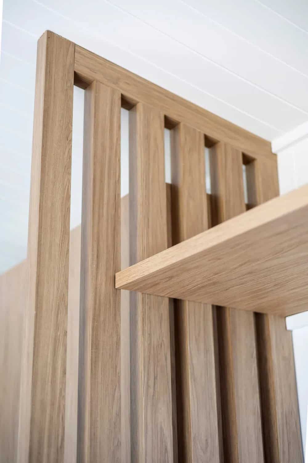 Close-up of the slatted timber screen in the Esther tiny house showing the floating shelf let into the frame and the fine joinery detailing against white VJ paneling