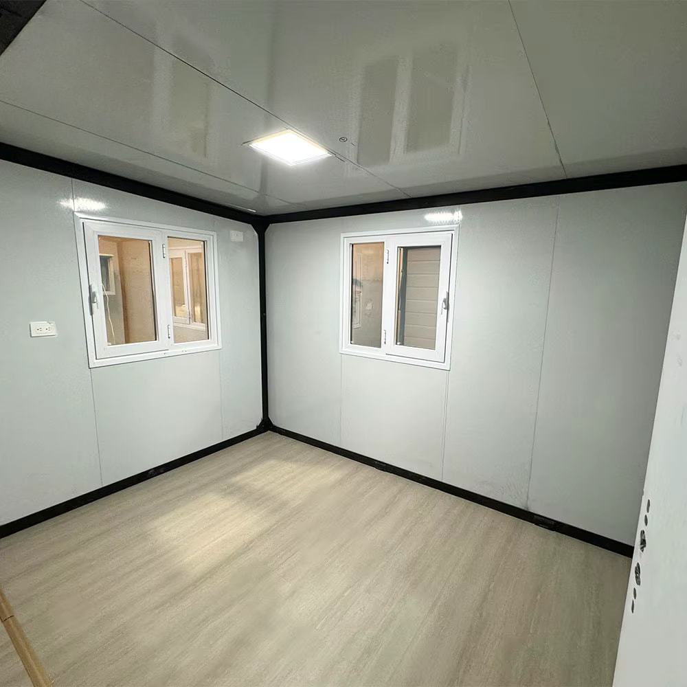 Interior of a tiny house with white walls, two windows, and a light wood floor.