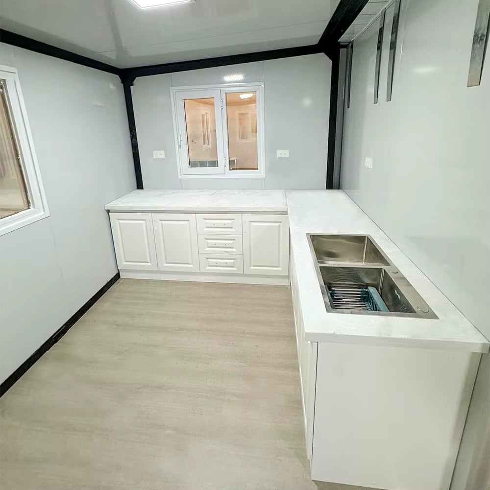 Compact tiny house kitchen with white cabinets and stainless steel sink.