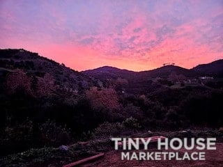 Scenic sunset over rolling hills with tiny houses in the distance.