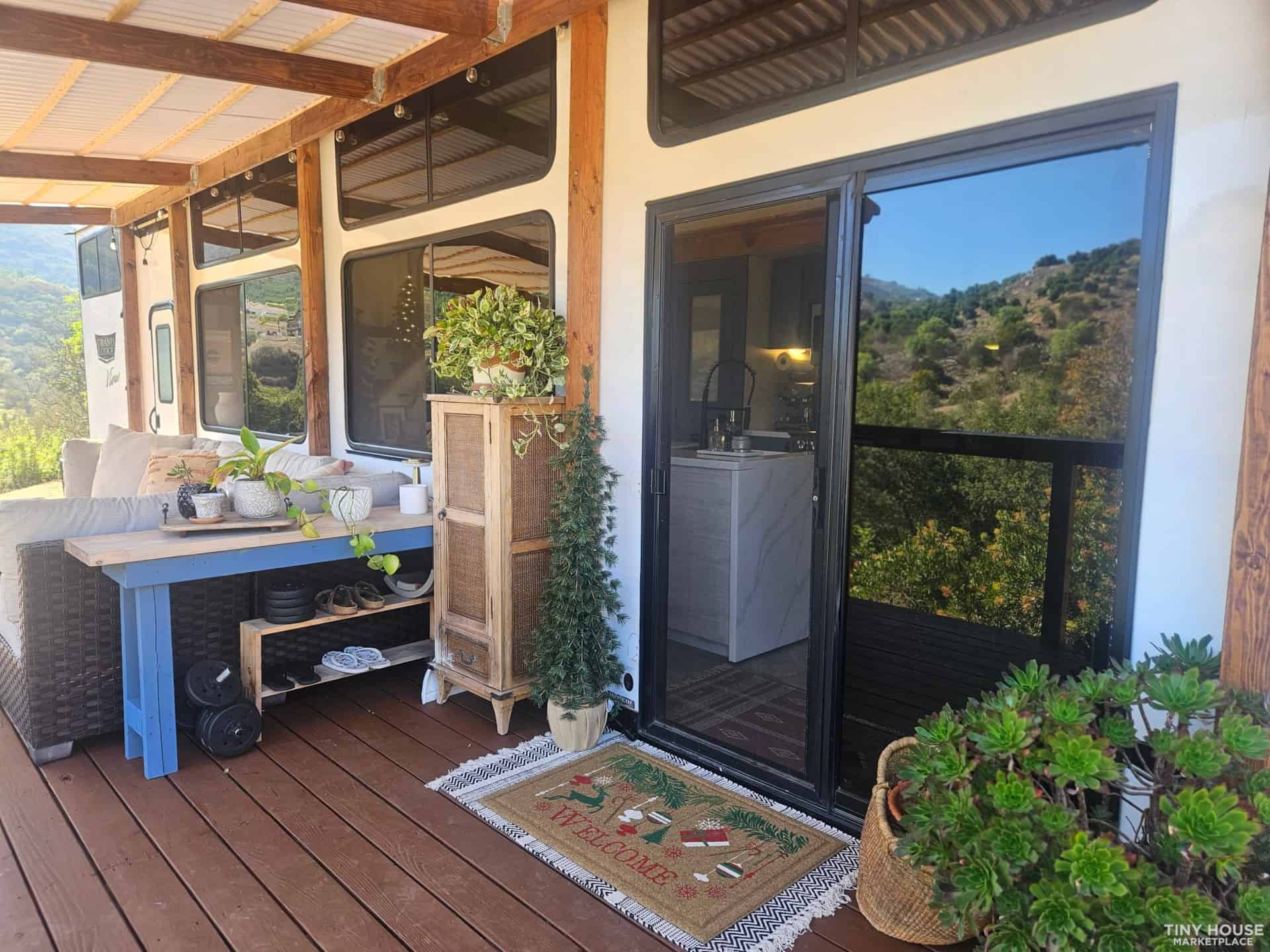 Charming tiny house porch featuring potted plants, a small outdoor table, and a welcoming entrance w.