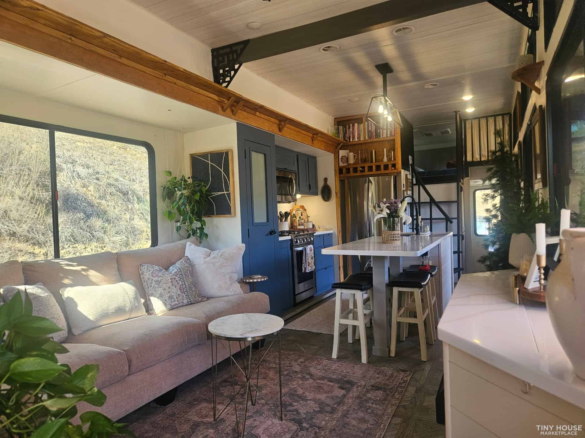 Full interior view showing living area, kitchen with navy cabinets, exposed wood beams, and two lofts on each end