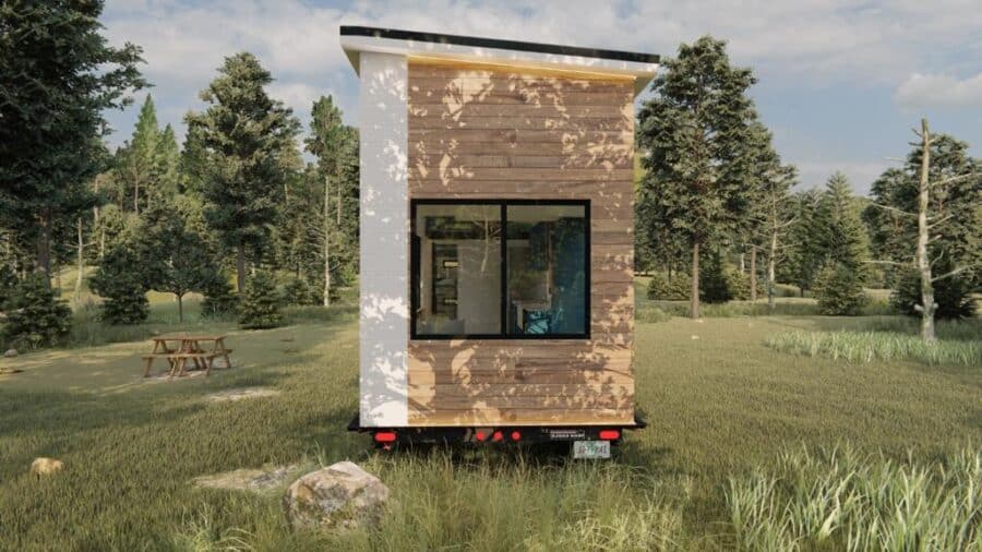 Small modern tiny house on wheels in a green outdoor setting.