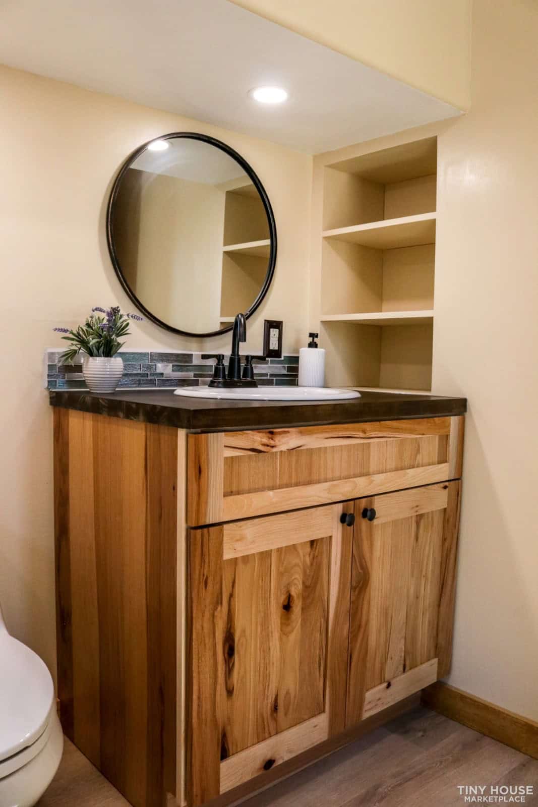 Hickory bathroom vanity with round mirror and built-in shelving