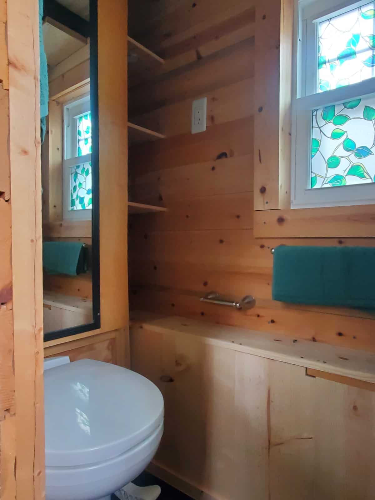 Tiny house bathroom with low-flush toilet, mirrored cabinet, open shelving and pine walls