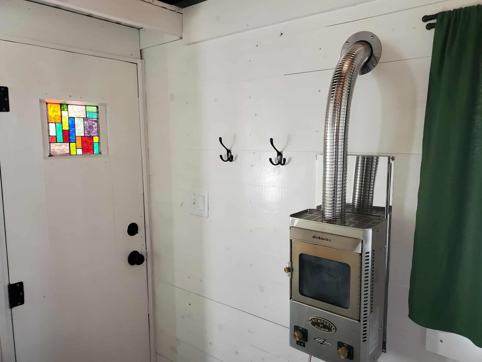 Entry door with inlaid stained glass panel beside a Dickinson Newport propane heater inside the tiny house