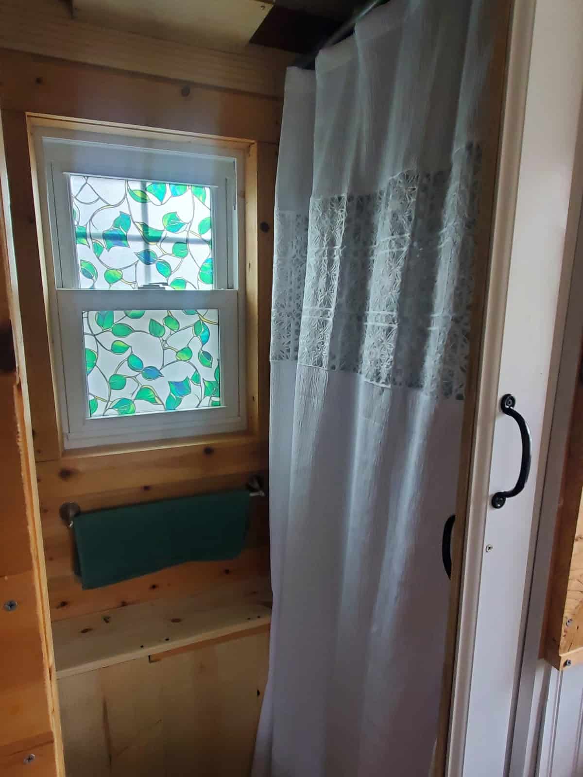 Shower area with curtain and decorative stained-glass-style privacy window in the tiny house bathroom