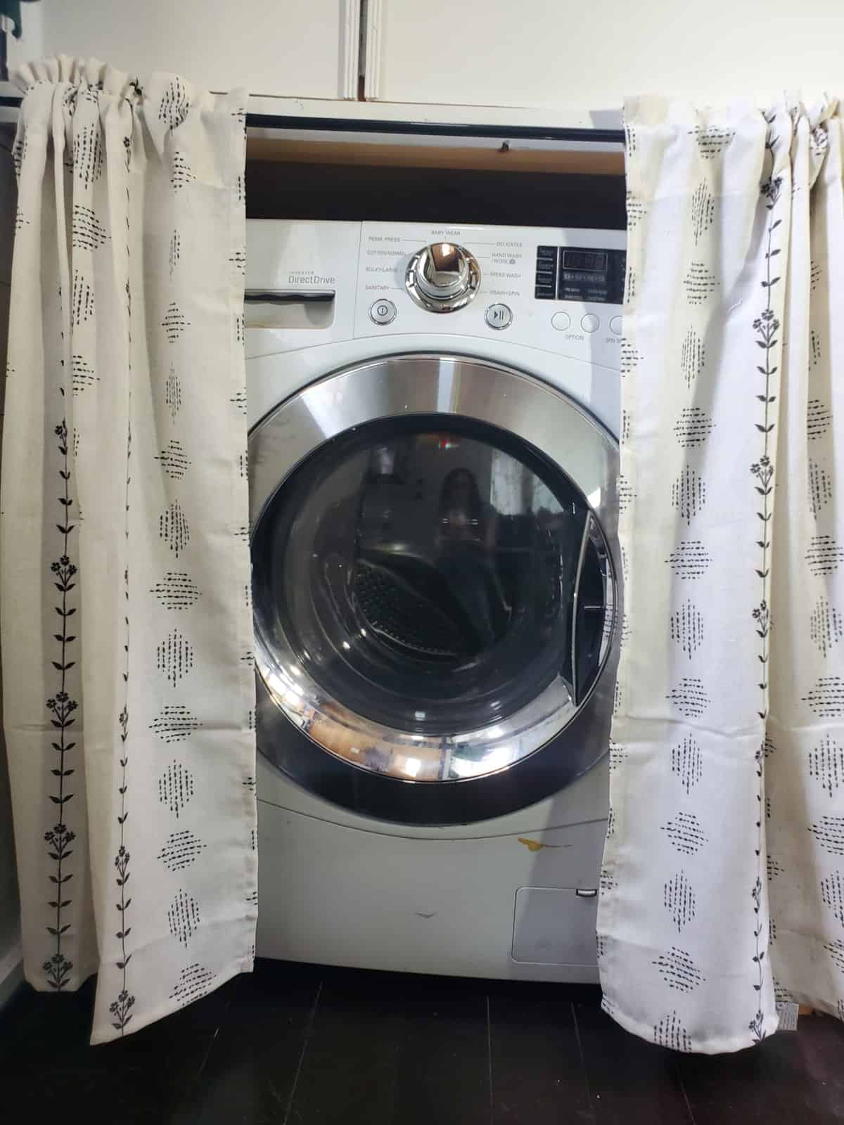 Full-size front-loading washer dryer combo tucked into a curtained alcove in the tiny house