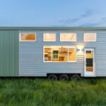 Modern farmhouse tiny house on wheels with large windows and sleek design.