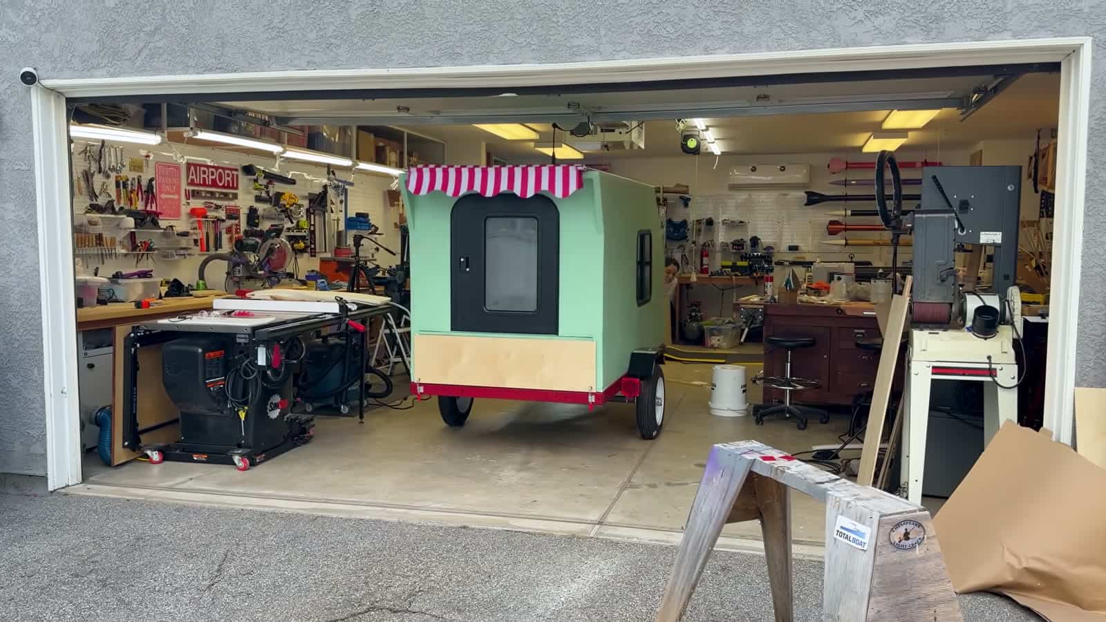 Finished foamie teardrop with striped awning parked in an open garage