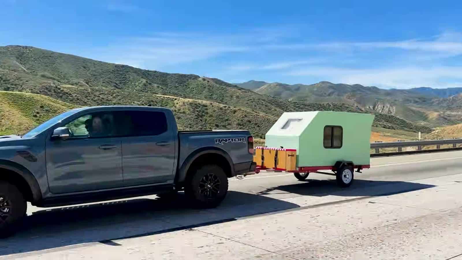 Pickup truck towing the mint green foamie teardrop down a mountain highway