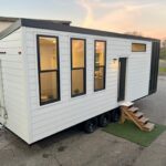 Contemporary tiny house on wheels with large windows and small staircase, ideal for compact living.
