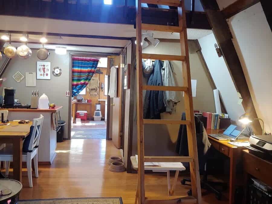 Cozy tiny house interior featuring a loft, kitchen, and workspace in a compact design.